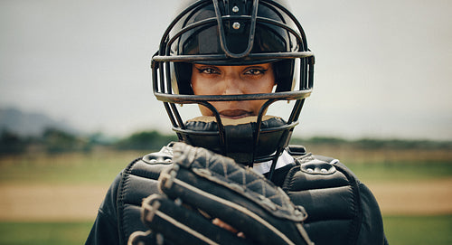 Focused female baseball player in catcher's gear poised to catch the ball on the field