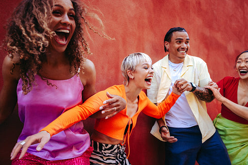 Laughing with friends while holding hands by a red wall outdoors