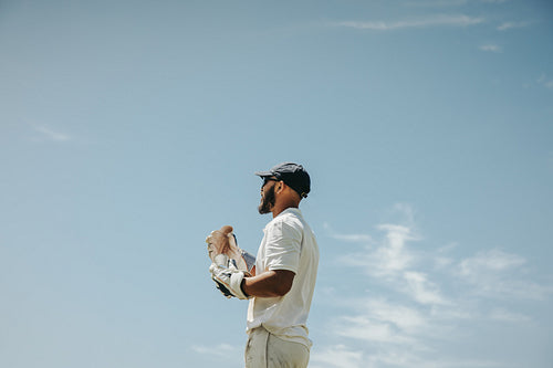 Male cricket player holding gloves under the clear blue sky