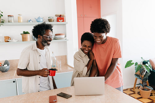 Teenage son using a laptop with his parents in their home kitchen