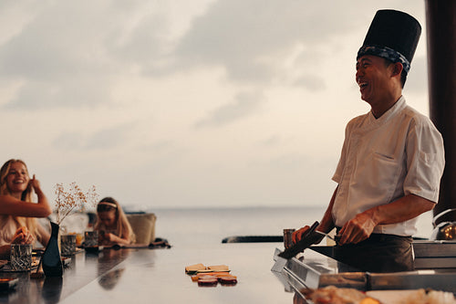 Chef entertaining guests during teppanyaki dining in an oceanfront restaurant setting
