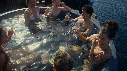 Group fun as friends enjoy drinks in an outdoor hot tub by the water