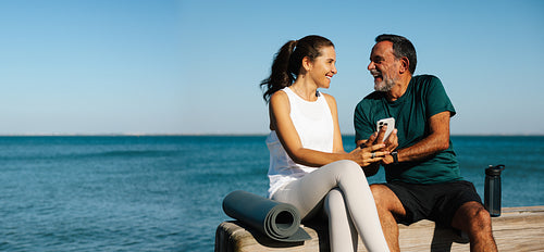 Senior man and woman smiling while sitting on a dock by the sea