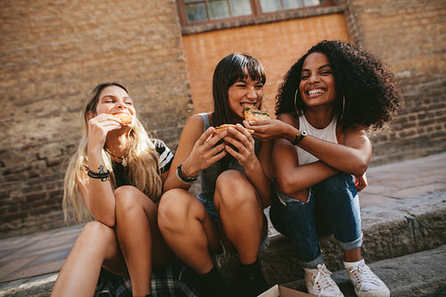 Young friends sitting on the sidewalk and having pizza