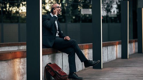 Businessman sitting outdoors talking over mobile phone