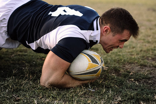 Strong rugby player with ball on ground