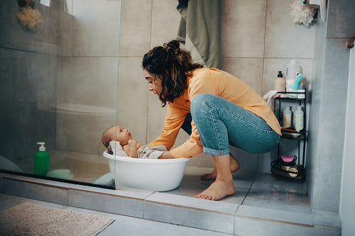 Mother bathes baby in tub at home