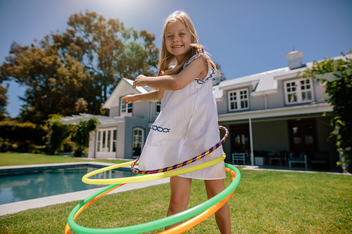 Little girl rotating hula hoop outdoors in her backyard
