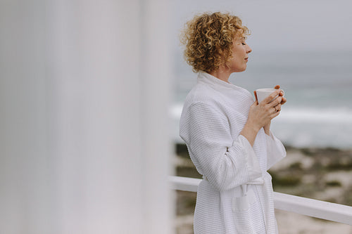 Woman enjoying coffee standing in the balcony of a beach house