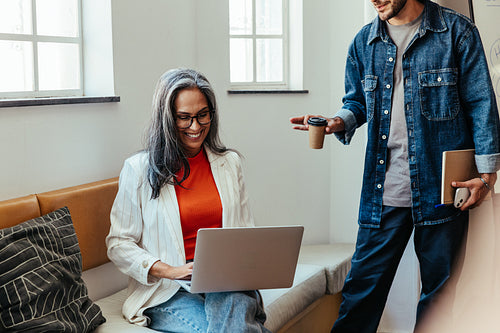 Business woman working on laptop with colleague in casual office setting