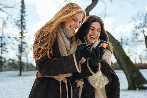 Women laugh over a smartphone outdoors in winter