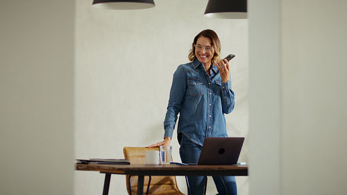 Cheerful business woman talking on phone and taking notes at desk