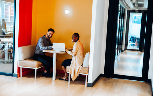 Two professionals discussing ideas while working at a booth seating area