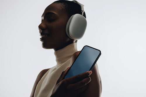 Woman with headphones holding smartphone for mockups and music streaming apps