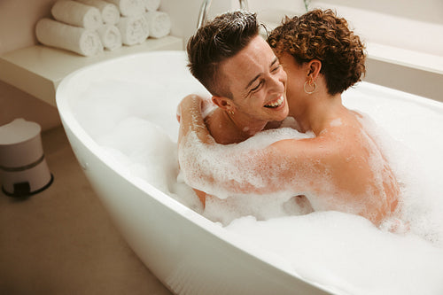 Smiling young queer couple enjoying a bubble bath together