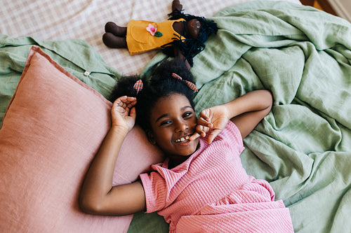 Cheerful black girl relaxing on bed, smiling and looking at camera