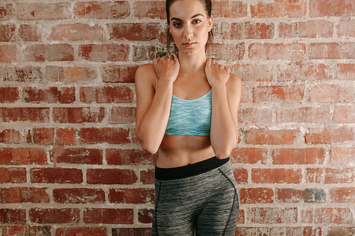 Beautiful woman in sportswear posing against brick wall
