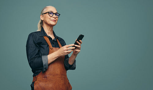 Modern jewellery maker holding a smartphone in a studio