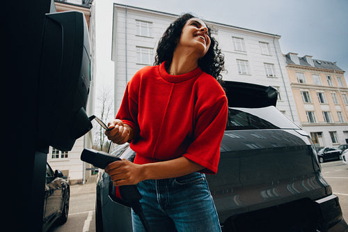 Woman charging electric car at public station outdoors