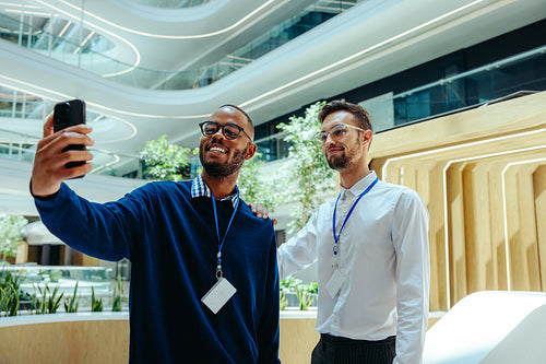 Two male colleagues taking a selfie in modern office space