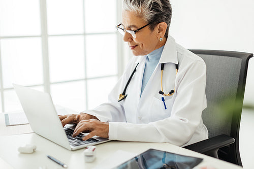 Senior female doctor using medical software on a laptop while working in her office