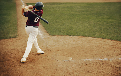 Batter executing a powerful swing, connecting with fly ball on baseball field during game