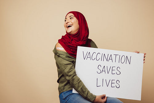 Cheerful muslim woman with banner of "Vaccination saves lives"