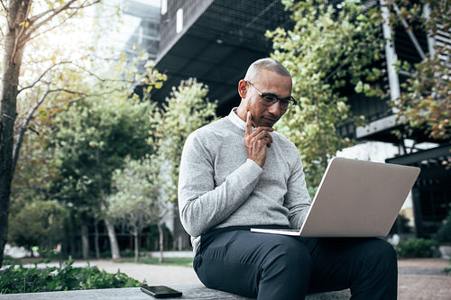 Businessman managing business working on laptop computer sitting outdoors