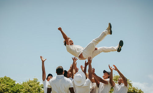 Cricket players celebrating a victory by lifting the man of the match in the air