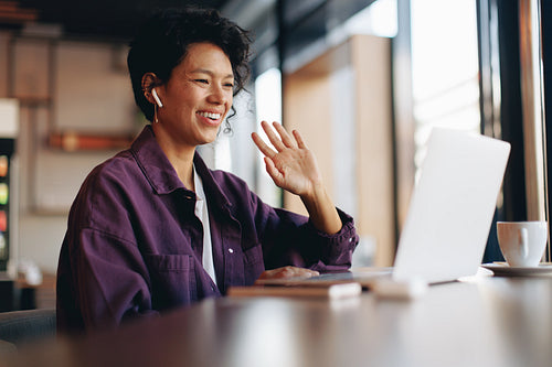 Freelancer waving during remote business meeting in a cafe with wireless earbuds