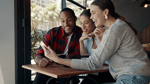 Group of friends looking at mobile phone and laughing at a coffee shop