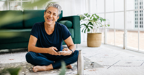 Taking a fitness break, happy mature woman sending a text message on her phone during yoga