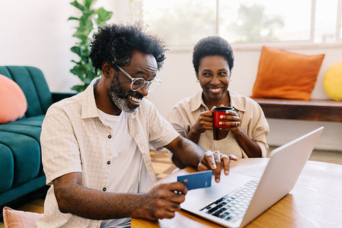 Cheerful black couple enjoying online shopping in their home