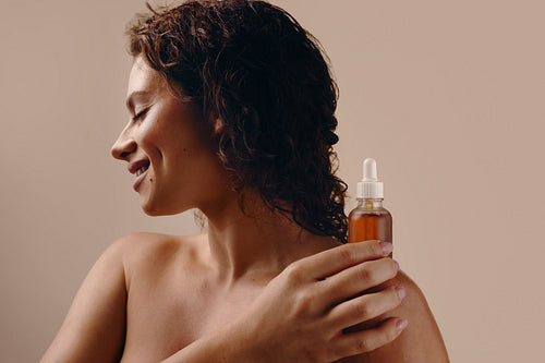 Smiling woman holding skincare serum bottle by her shoulder