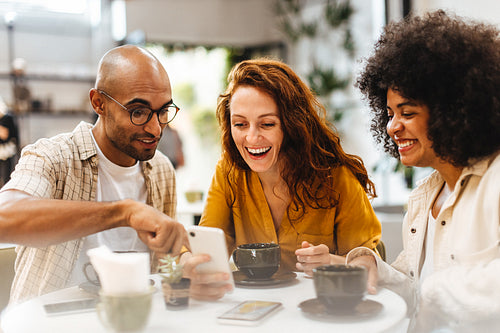 Group of friends using a phone as they have coffee in a cafe