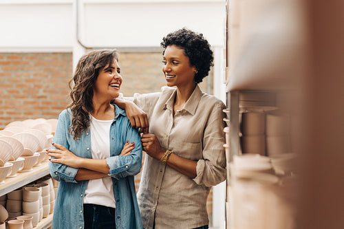 Cheerful businesswomen smiling at each other in their ceramic store