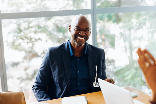 Smiling businessman seated at desk holding eyeglasses during a meeting
