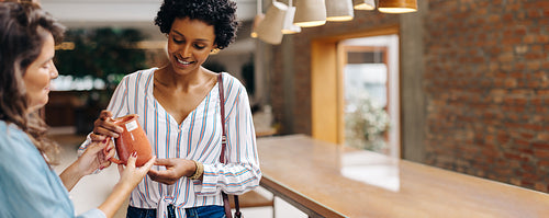 Ceramic shop owner showing an earthenware product to a customer in her store