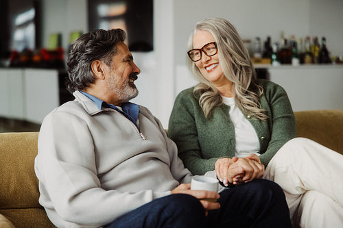 Senior couple holding hands on a sofa at home