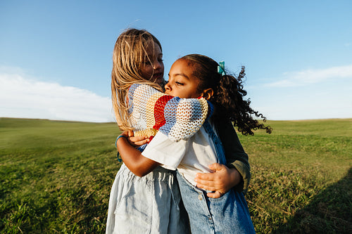 Girls hug in sunny field.