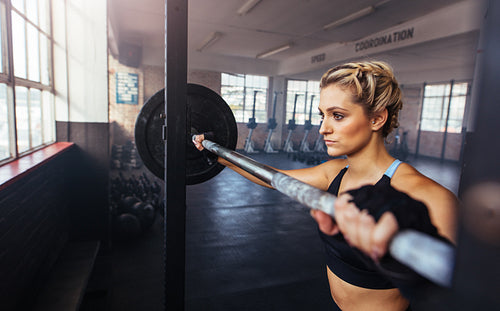 Young woman working out at the gymnasium using weight bar.