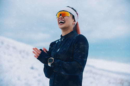 Joyful female athlete in winter sportswear laughing in snowy landscape