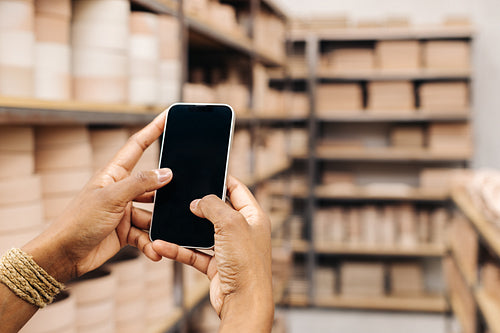 Unrecognizable ceramist using a smartphone in her shop