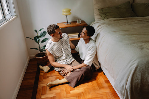Male couple sitting affectionately together on a wooden floor at home