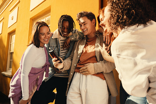 Group of friends laughing and enjoying a moment while looking at a smartphone outdoors