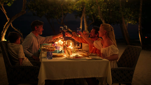 Joyful family and friends enjoying a beautiful candlelit dinner at an island resort at night