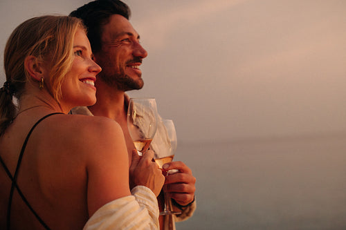Young couple enjoying serene sunset with glasses of wine, embracing peaceful moments