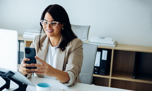 Office day: woman smiling while using phone and tablet