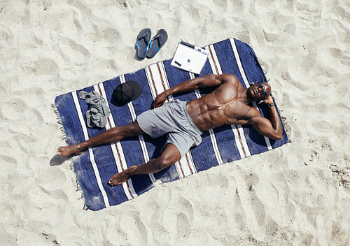 Young man relaxing on mat at beach