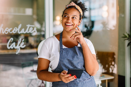 Female entrepreneur standing in her cafe, smiling pensively